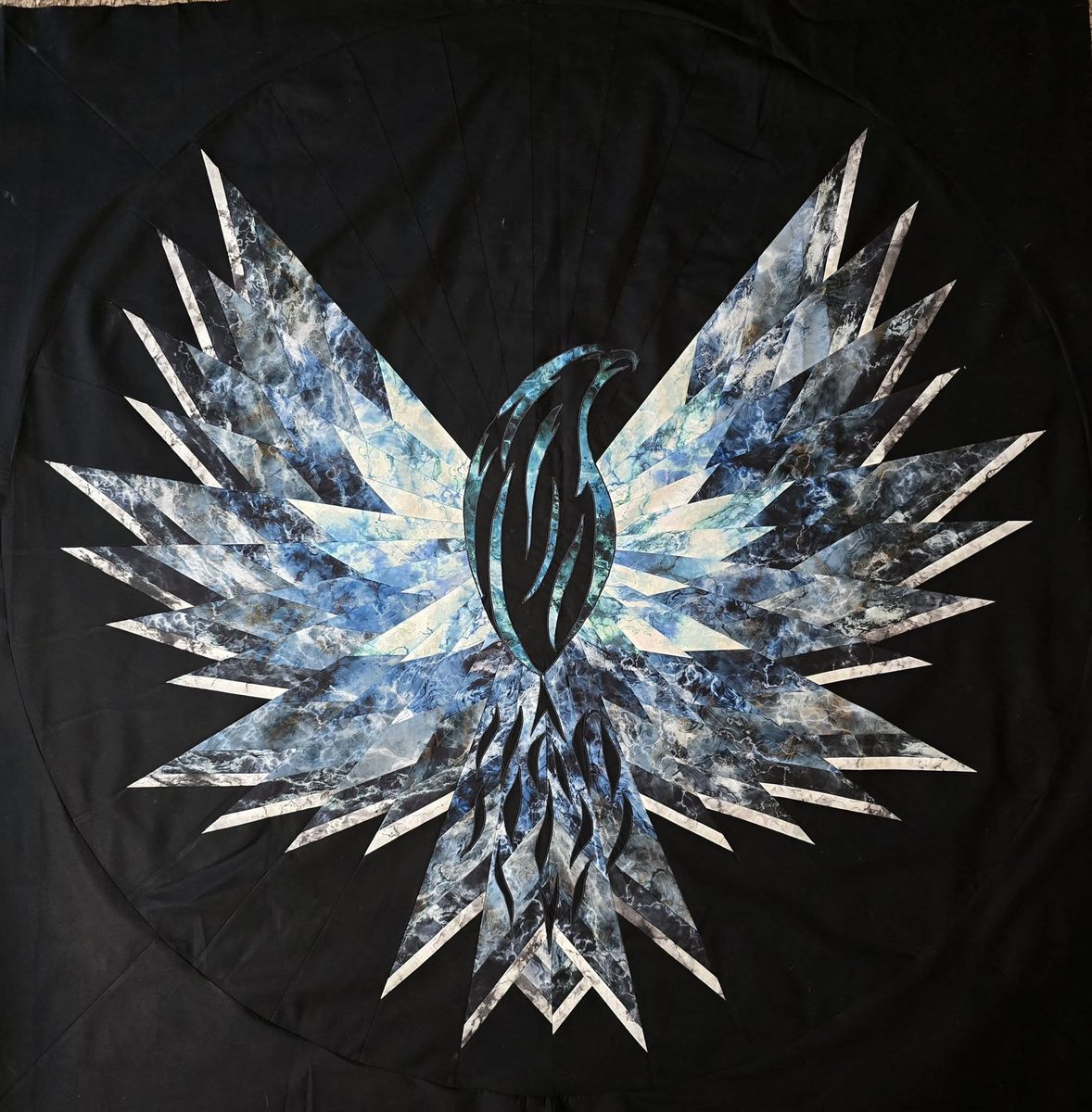 A quilt of outstretched wings in blues, greys and white, pieced from hundreds of sharp feather shapes against black
